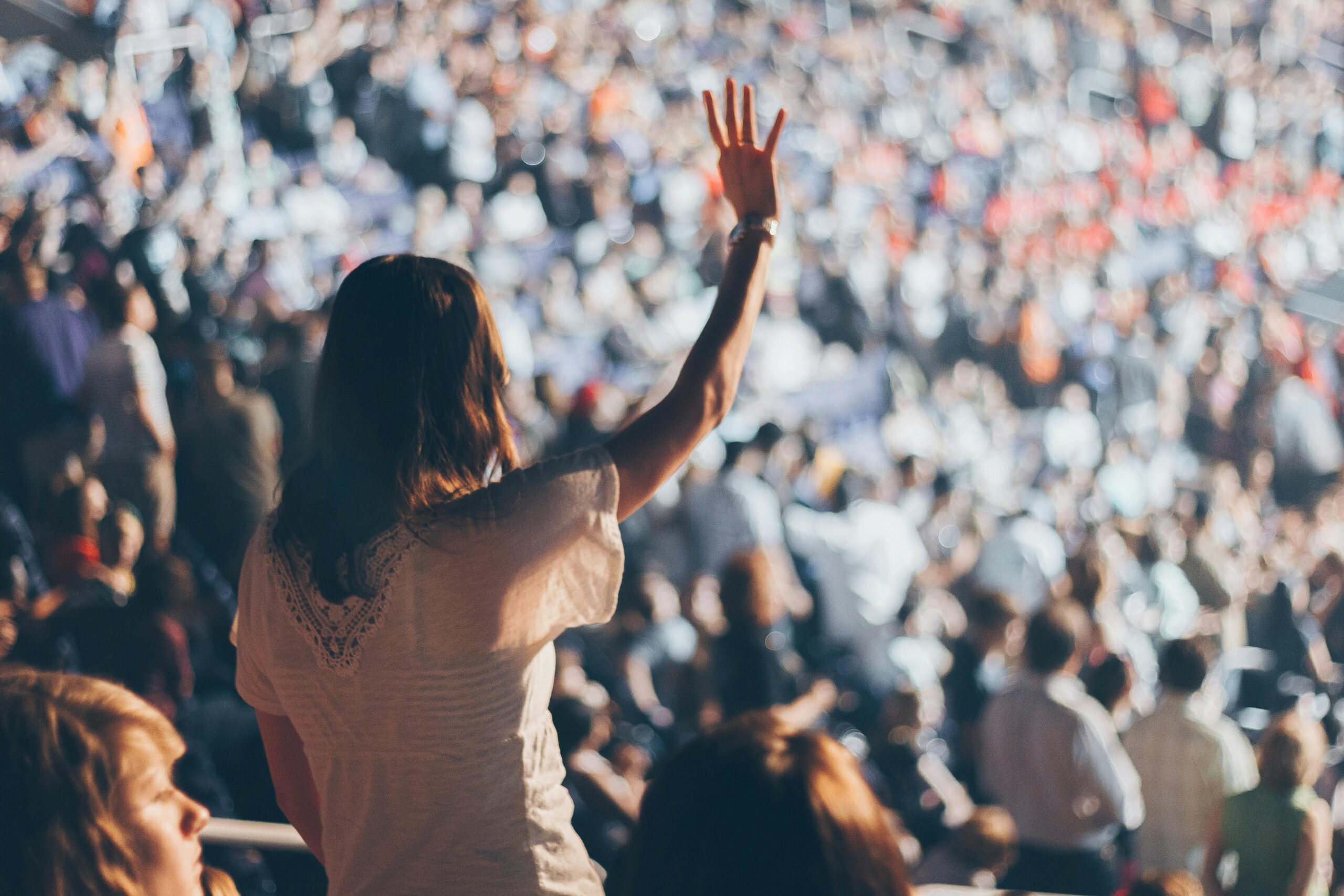 Diverse crowd enjoying a live event with one woman raising her hand in excitement.